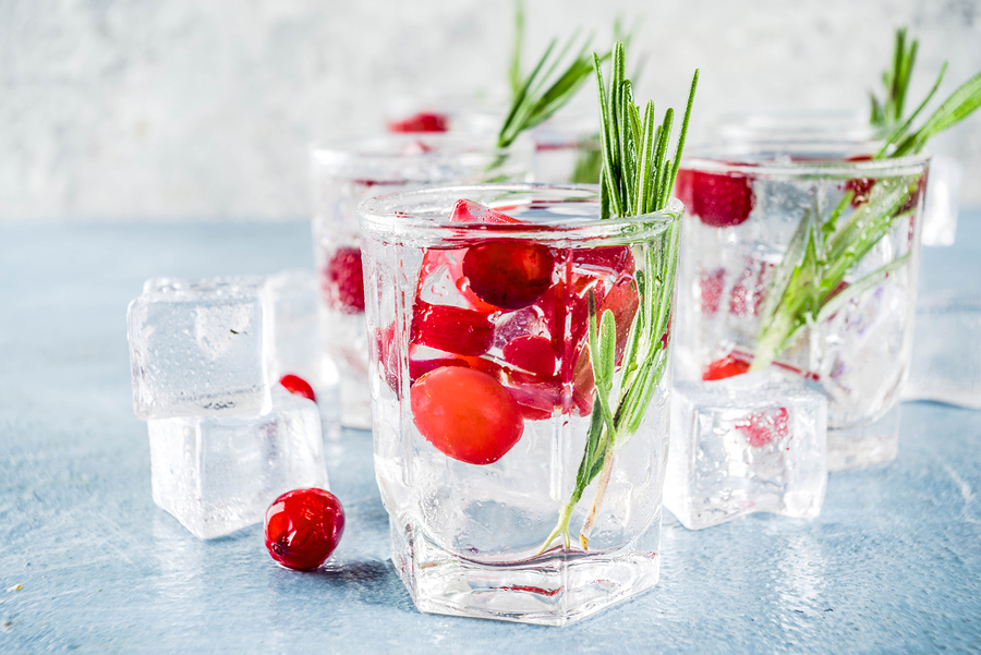 Christmas or New Year winter cranberry cocktail with rosemary, liqueur, gin tonic, on light blue concrete background with ice cubes, fresh berries and rosemary twig copy space