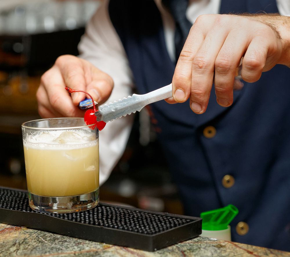 Bartender is decorating whisky sour cocktail with cherry